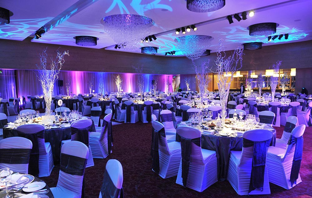 Gala dinner banquet hall with white chair covers, purple sashes and uplighting